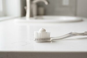 White toothbrush with a dollop of toothpaste on the bristles on a white bathroom counter.