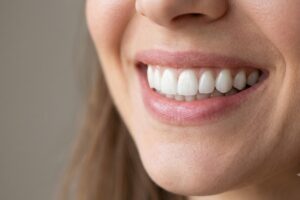 Close-up of a smiling mouth showing white teeth and pink lips, lower face visible in soft light.