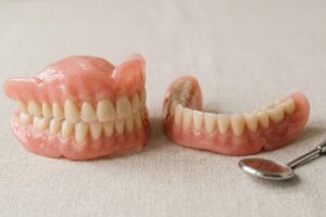 Pair of pink acrylic dentures (upper and lower) placed on a beige fabric with a dental mirror nearby.