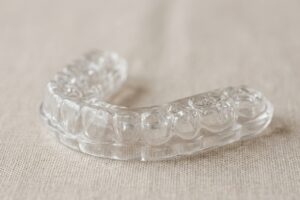 Transparent dental aligner tray resting on a beige fabric surface for teeth straightening treatment.