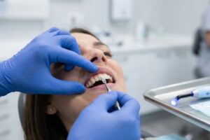 Dentist in blue gloves treats a patient's teeth using a dental instrument in a clinical setting.