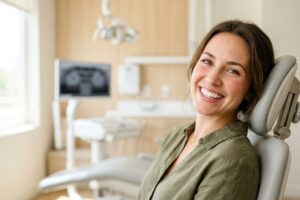 Smiling woman seated in a dental chair at a modern clinic, looking at the camera.